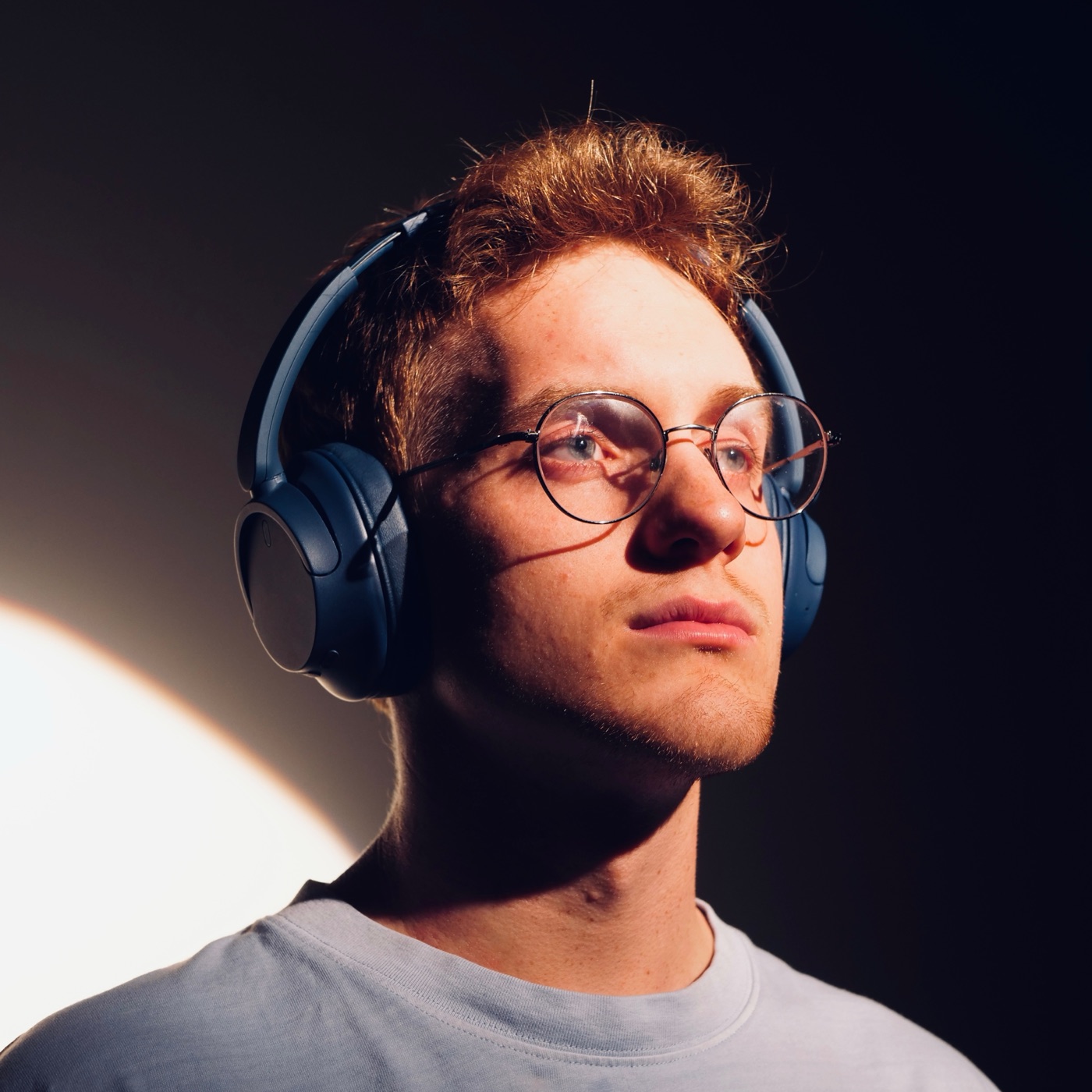 Kosta in round glasses and blue headphones, lit from the side